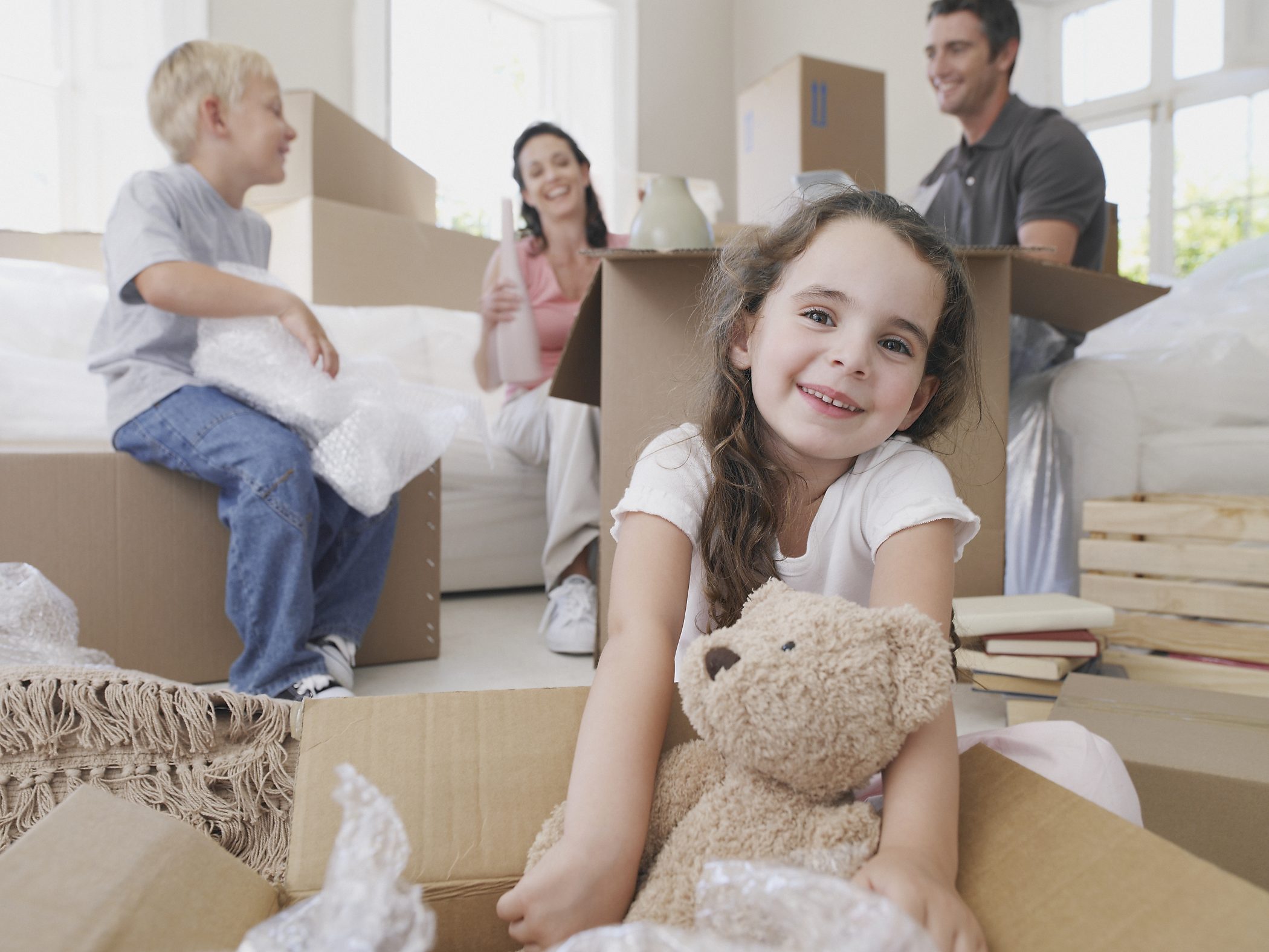 Girl with teddy bear in cardboard box with brother and parents in background